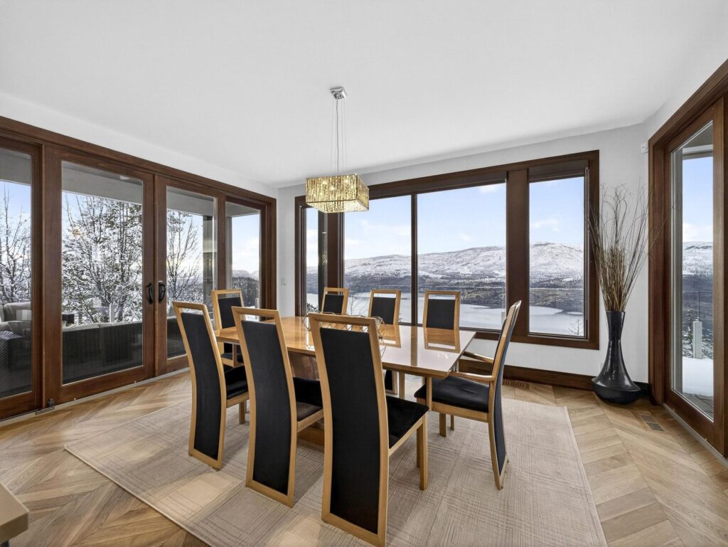 Dining room seating eight, framed by tall windows on two sides looking out to snow-covered hills.