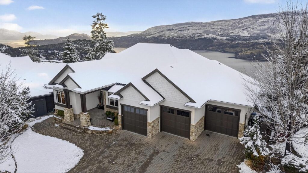 Front of a house with a snow-covered roof and a triple garage, photographed from above in winter.
