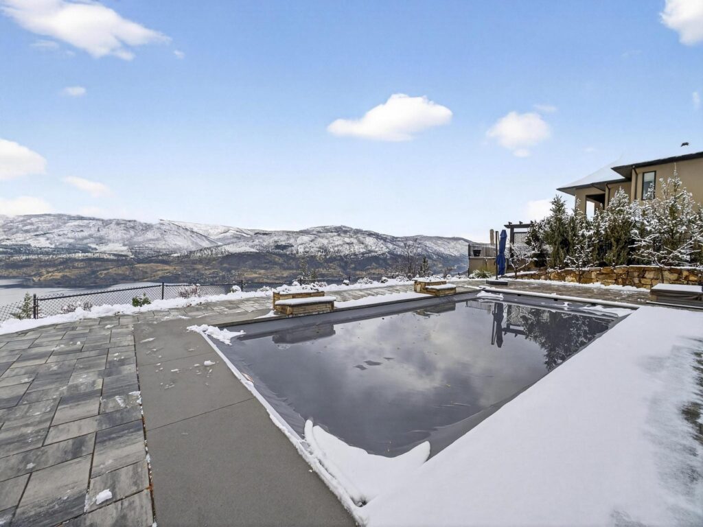 Dark-bottomed pool on a snow-edged terrace, with Okanagan Lake and the far shore behind it.