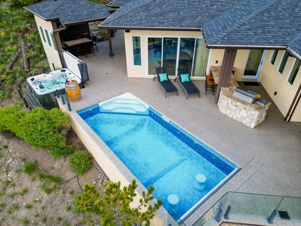Aerial view straight down onto a rectangular pool, a hot tub and loungers on a terrace beside the house.