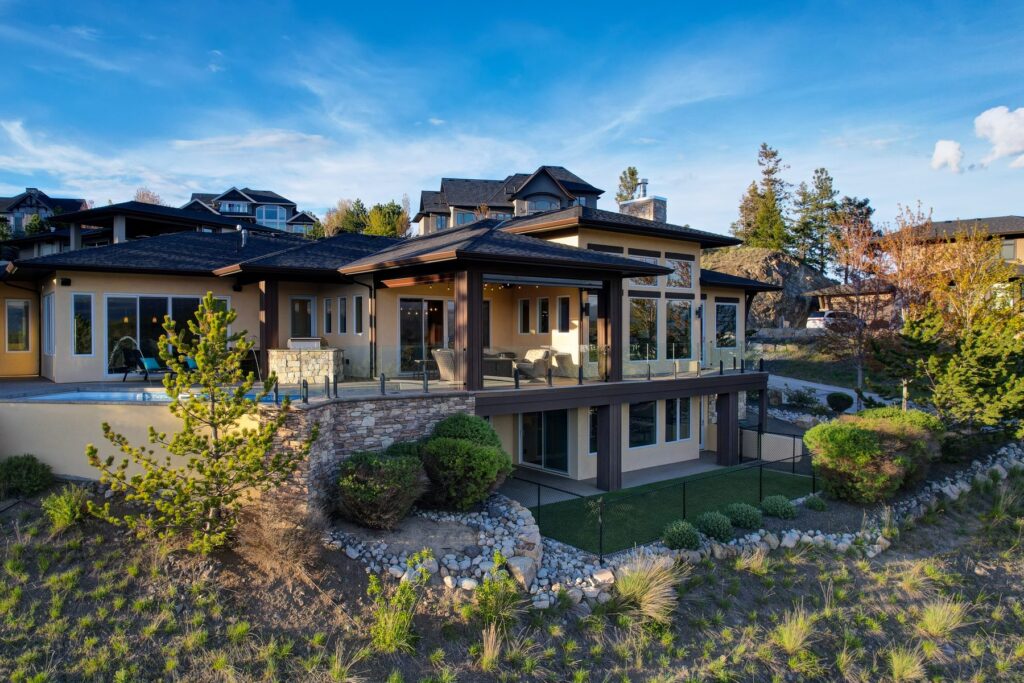 Rear of a contemporary home in daylight, with wide glazing, a covered patio and a stone retaining wall along the slope.