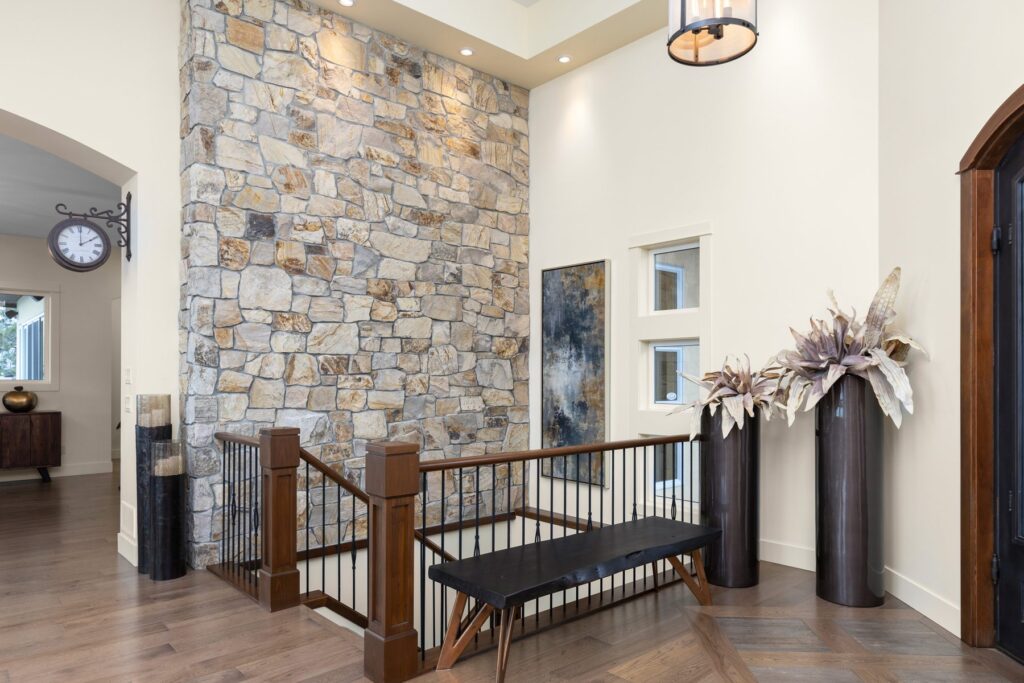 Double-height entry with a full-height stone chimney breast, a wood and iron stair rail, and a pendant light.