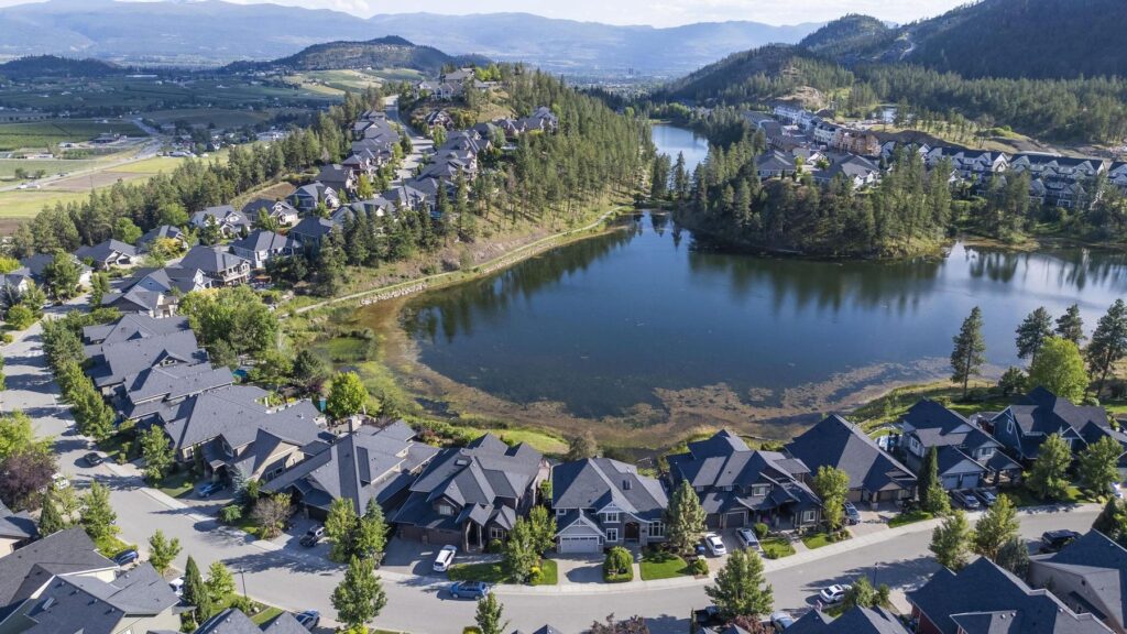 Aerial view of houses arranged around a small lake, with dry hills and mountains behind.