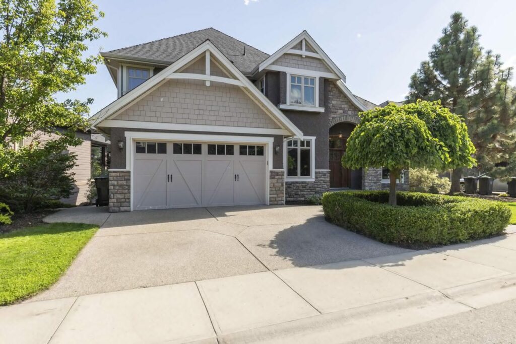 Front of a two-storey home with stone and shingle cladding, a double garage and a clipped topiary beside the door.