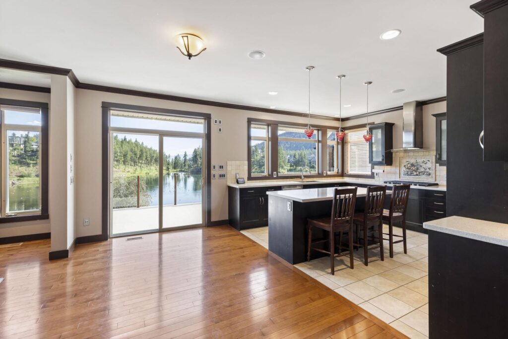 Kitchen with dark cabinets and a raised breakfast bar, opening to a bare living area and sliding doors onto water beyond.
