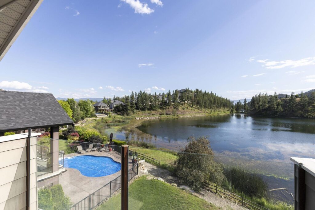 A small pool behind a glass fence in the foreground and a still lake ringed by hills stretching away behind it.