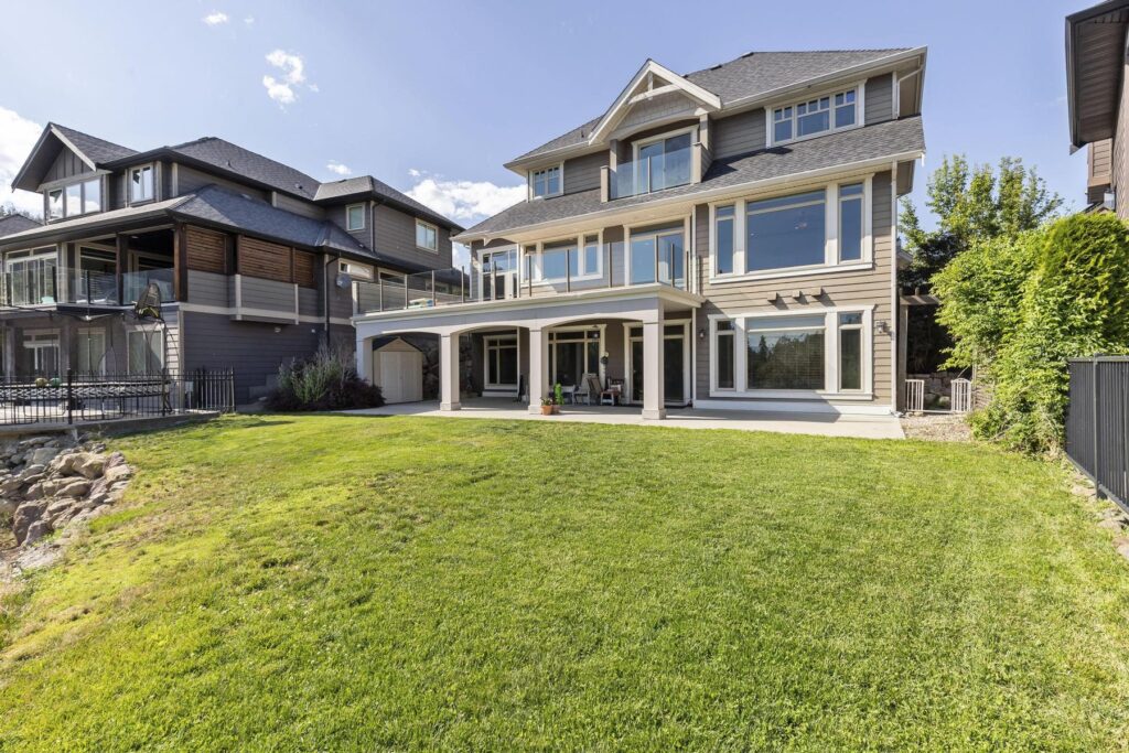 Rear of the house across a sloping lawn, with a columned covered patio and stacked balconies above it.