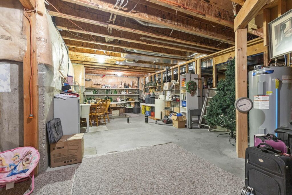 The same unfinished basement from the other end, showing the hot water tank, a workbench and stored boxes under open joists.