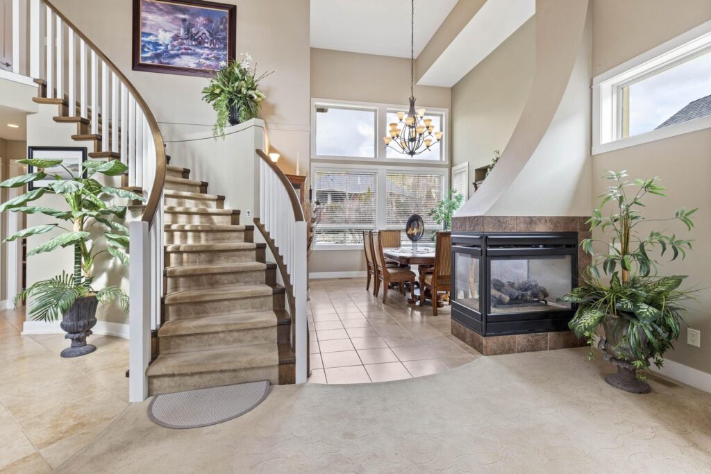 Entry hall with a curved carpeted staircase, a tiled floor and a see-through fireplace into the dining area.