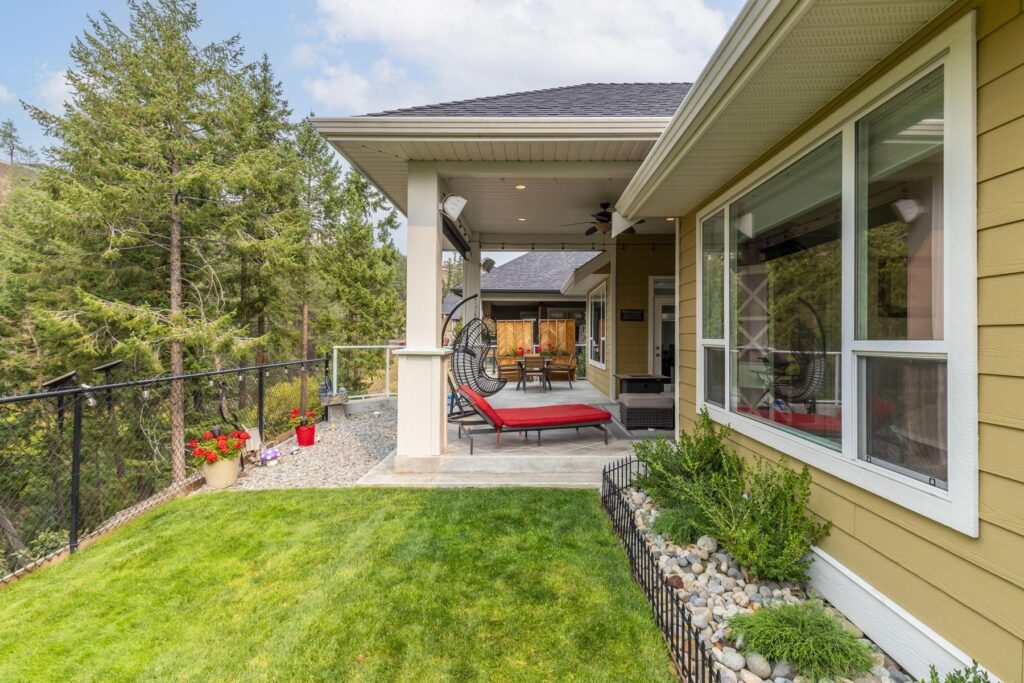 Covered patio with columns and red loungers beside a fenced lawn, backing onto mature pines.