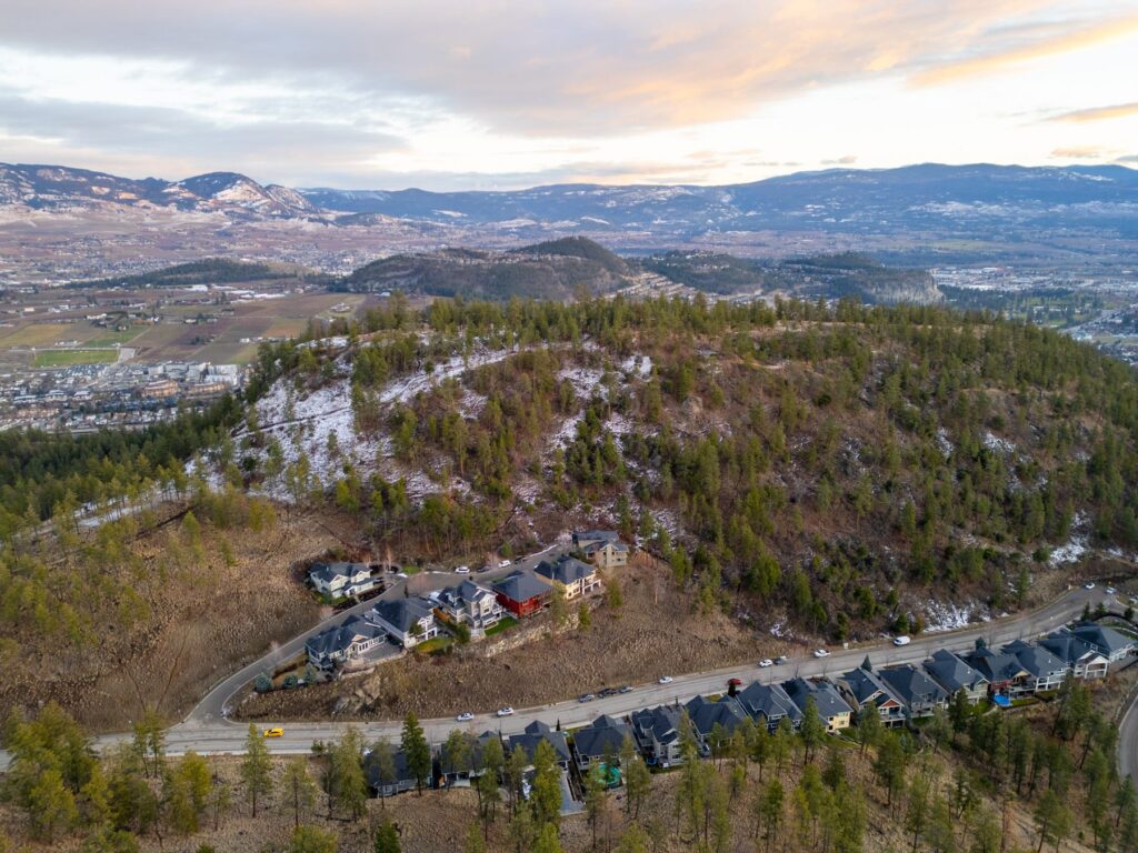Aerial view of a hillside subdivision below a rocky bluff in early spring, with the valley and a lake beyond.