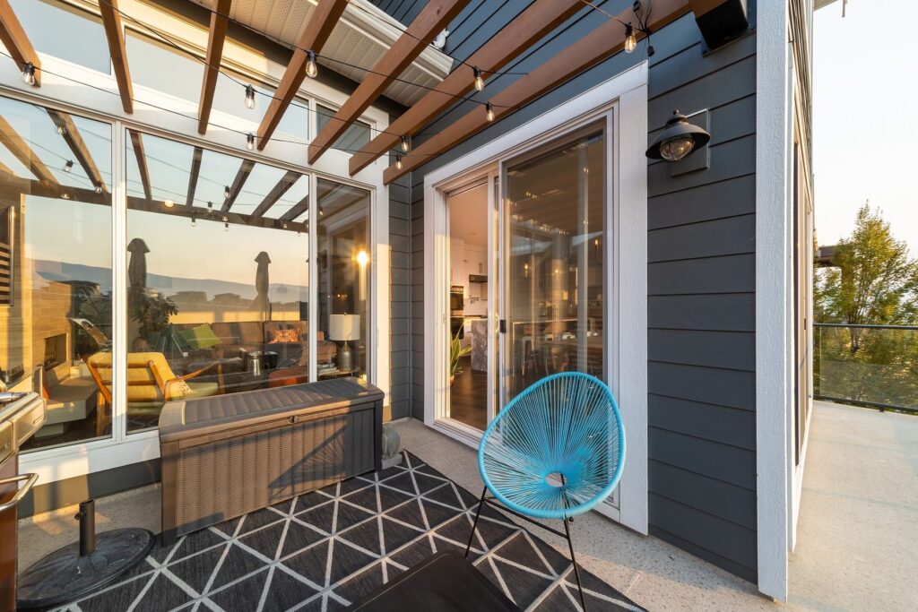 Covered deck under a timber pergola in low evening light, with a patterned rug, a blue chair and the valley beyond.