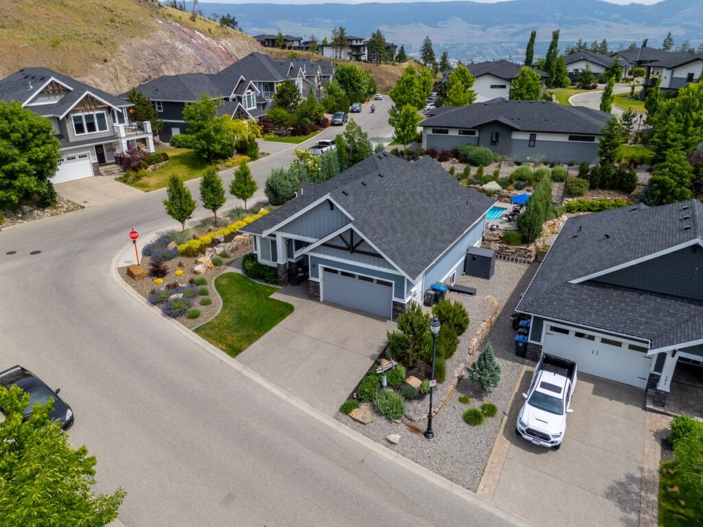 Aerial view of a house on a quiet suburban street, with a landscaped front garden and hills rising behind the neighbourhood.