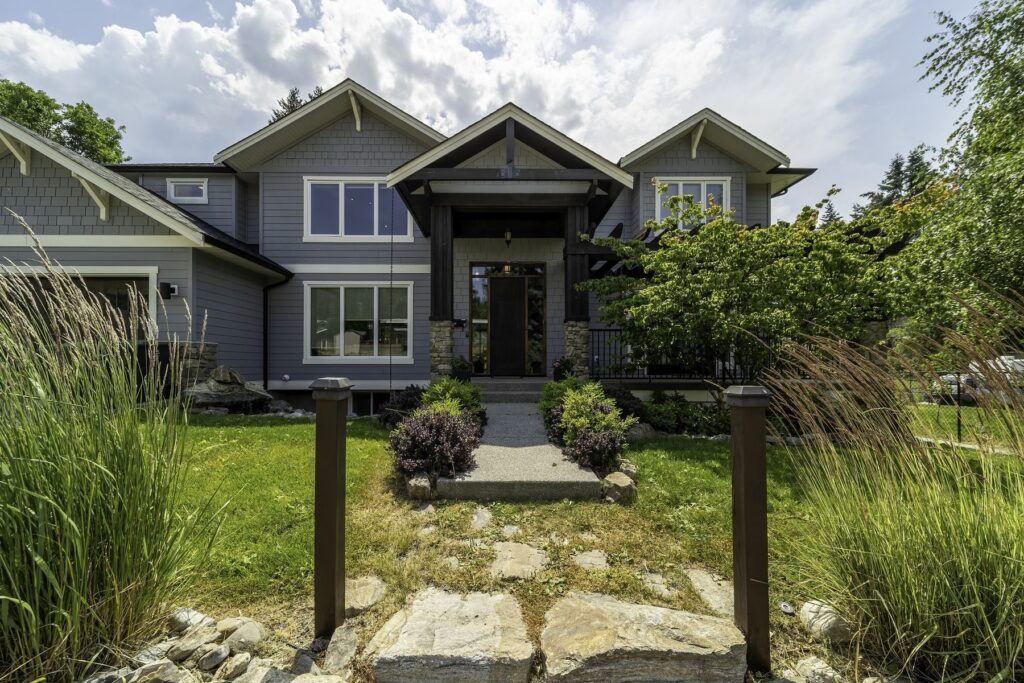 Front of a grey two-storey home with a covered entry, approached by a stone path through ornamental grasses.