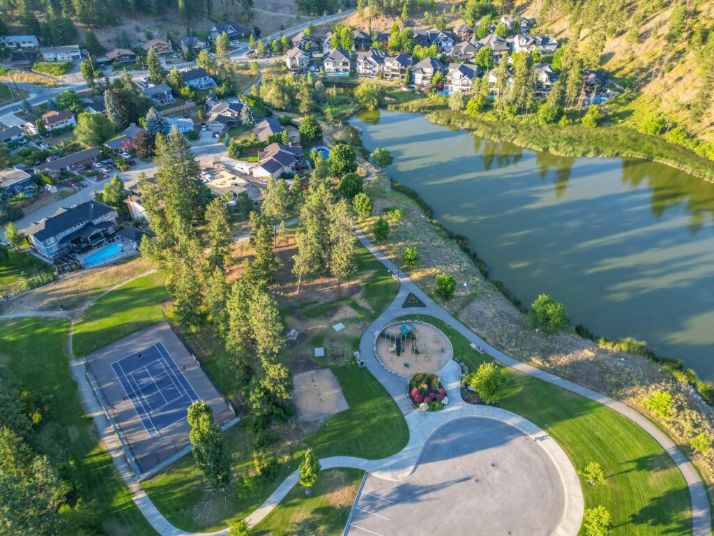 Aerial view of a neighbourhood park with a pond, tennis courts and a looping footpath.