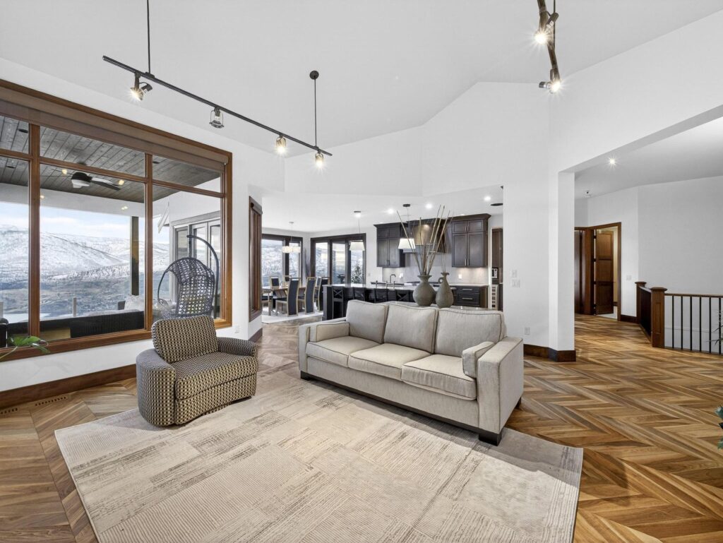 Bright open living area with a sectional sofa, herringbone wood floors and a wall of windows facing snow-covered hills.