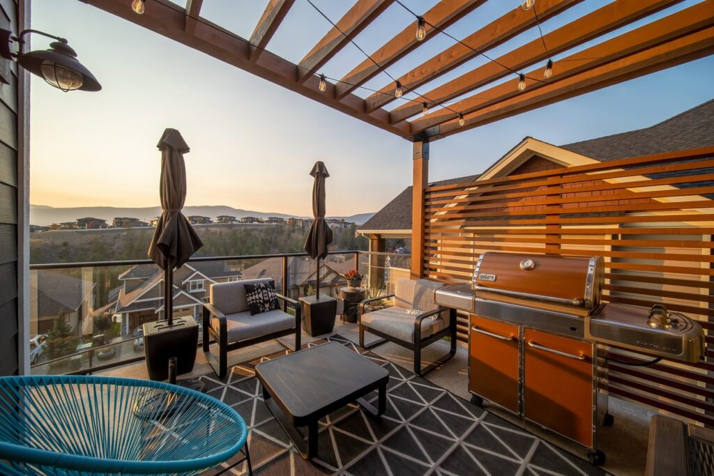 Outdoor kitchen and seating under a timber pergola at sunset, with umbrellas closed and the valley behind.