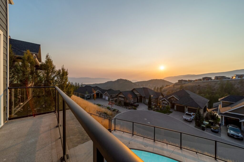 The sun setting behind distant hills, photographed over a deck railing with the pool and rooftops below.