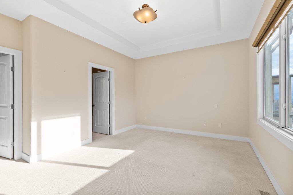 An empty carpeted bedroom with a window, a closet door and no furniture.