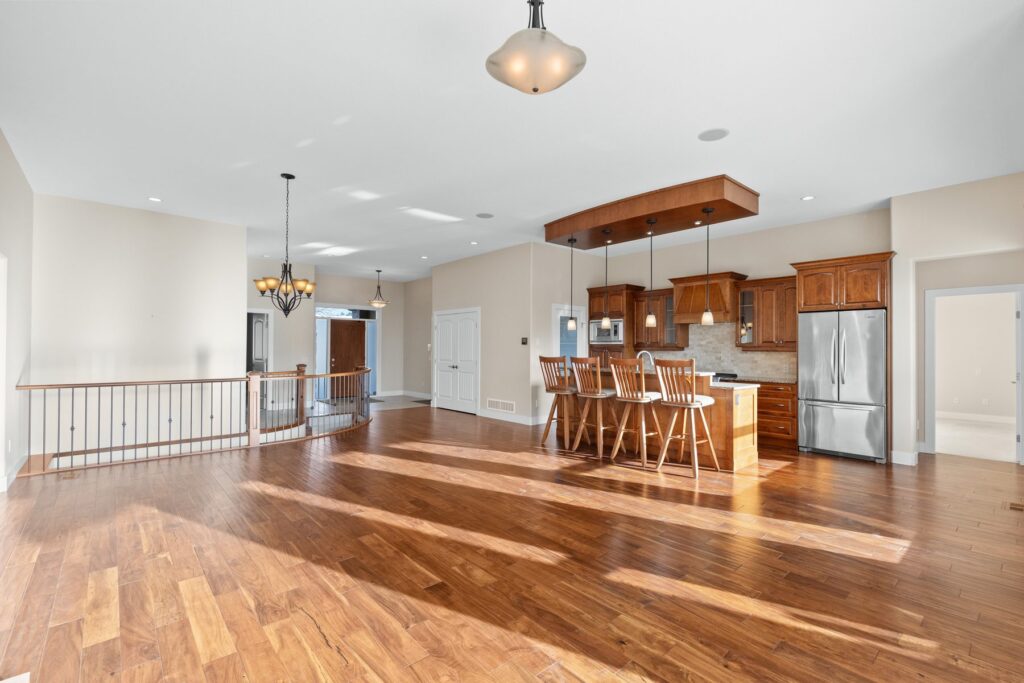 An empty open-plan living and kitchen area with bare hardwood floors, a stair railing and no furniture.