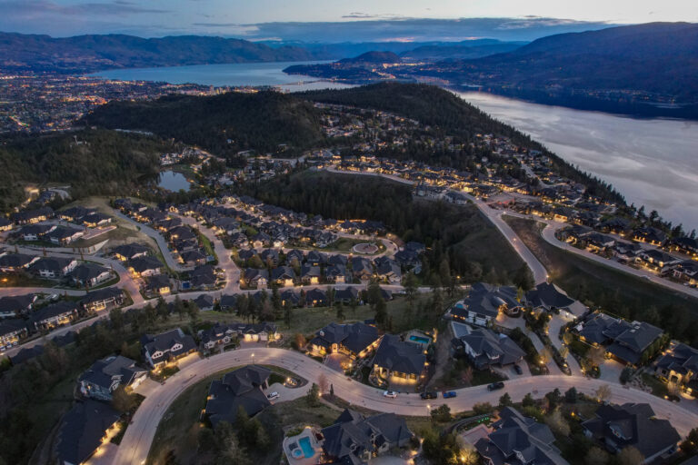 Aerial view of Kelowna at dusk, hillside homes above Okanagan Lake with the city lit beyond