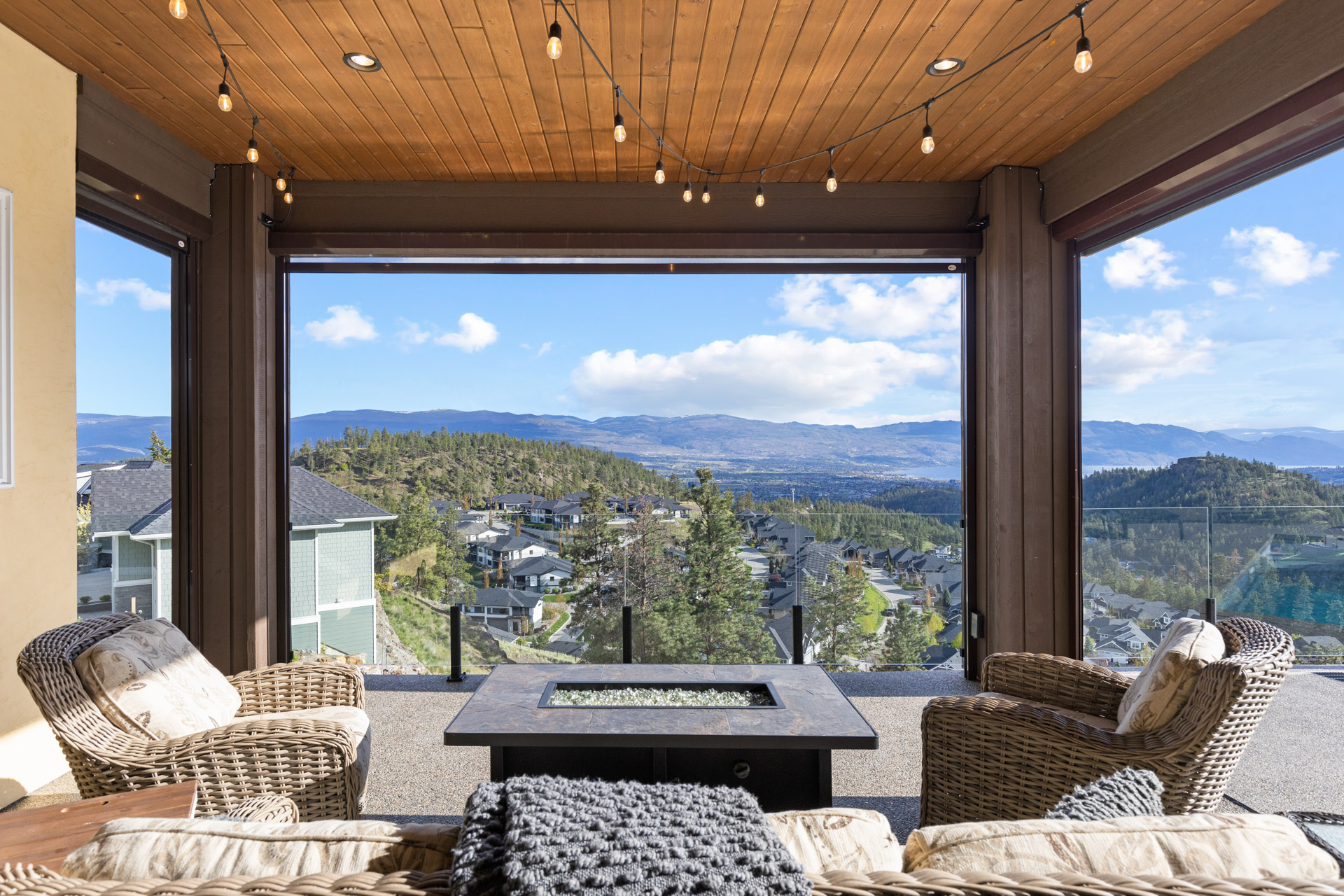 Covered patio with a fire table looking over a Kelowna hillside neighbourhood and the valley beyond