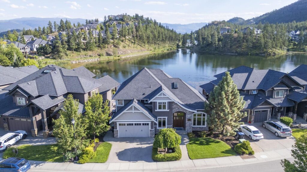 Homes along the shore of Hidden Lake in Wilden, Kelowna, seen from the air, with more houses and the treed ridge of the Glenmore Highlands behind